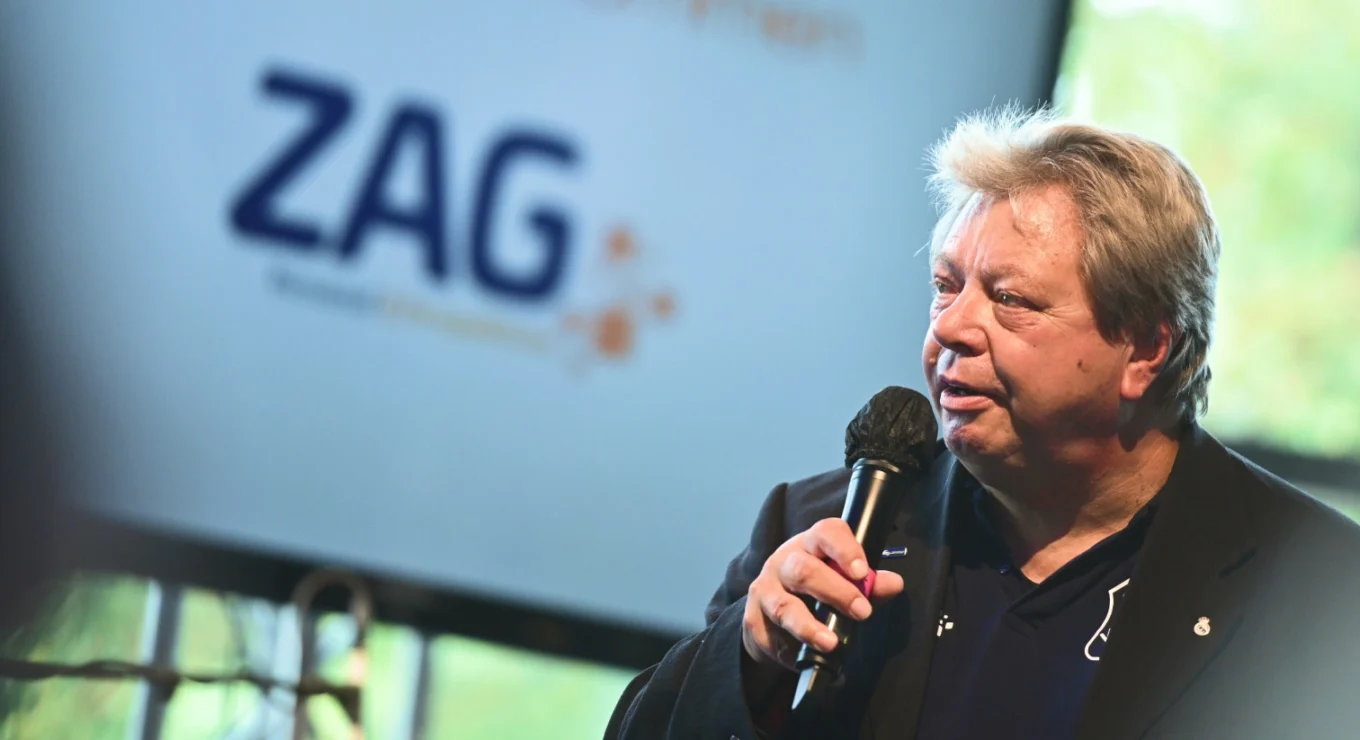 Hochwertiges Foto eines Mannes bei einer Rede vor einer ZAG-Veranstaltung, Fokus auf den Sprecher mit ZAG-Logo im Hintergrund, Symbol für professionelle Personaldienstleistungen und innovative Personalvermittlung.