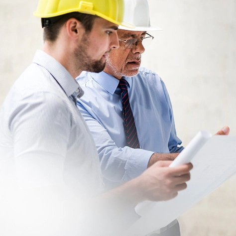 Zwei Bauingenieure mit Helmen prüfen Baupläne auf einer Baustelle für effiziente Projektumsetzung.