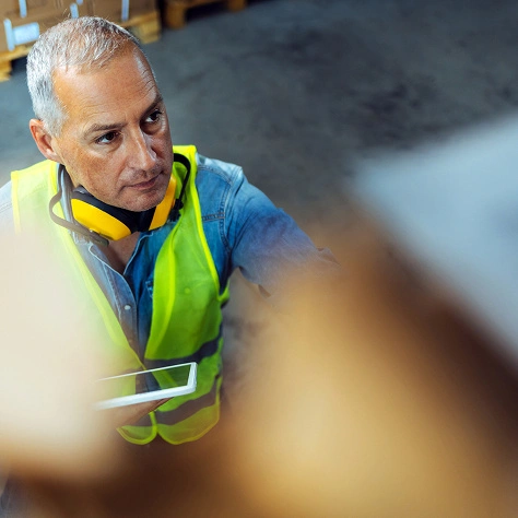 Mann im Sicherheitsweste mit Schutzkopfhörern bei Arbeit.