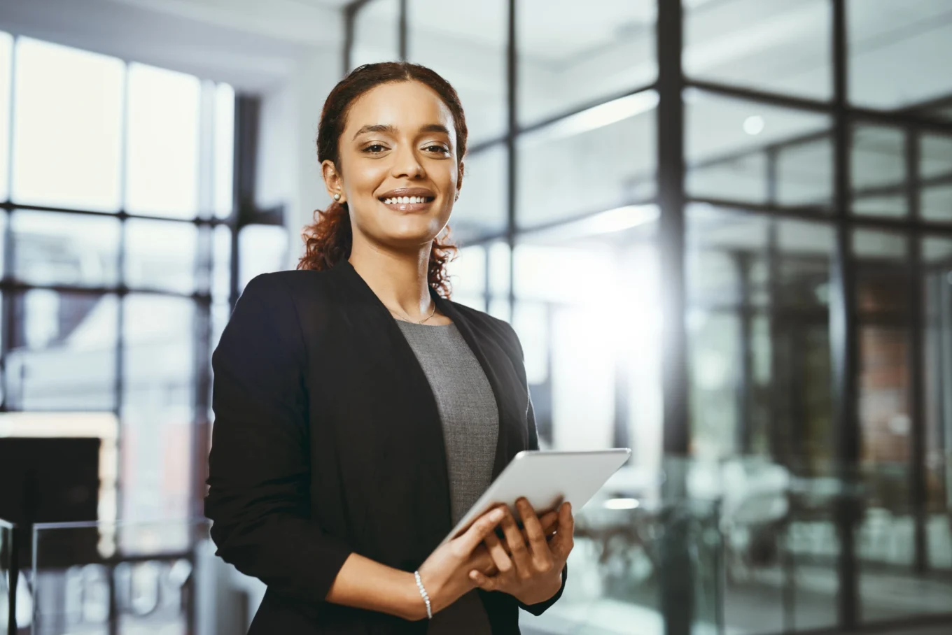 Moderne Geschäftsfrau in einem Business-Umfeld hält Tablet, symbolisiert Professionalität und Innovation im modernen Arbeitsumfeld.