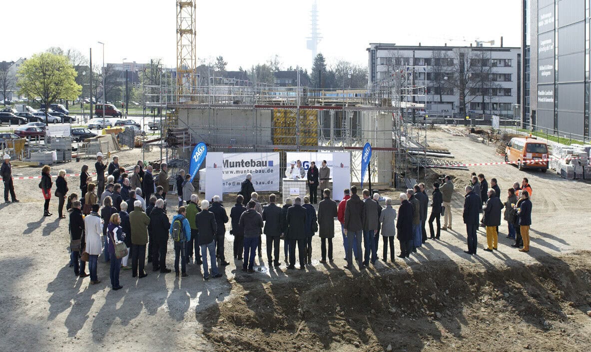 Baustelleneinweihung bei ZAG in Deutschland mit Bauarbeiten, Gruppe von Gästen und Bauleitern, Baukräne und Gerüste, modernes Projekt, Immobilienentwicklung, nachhaltiger Bauprozess, ZAG Logo sichtbar, Stadtumfeld.