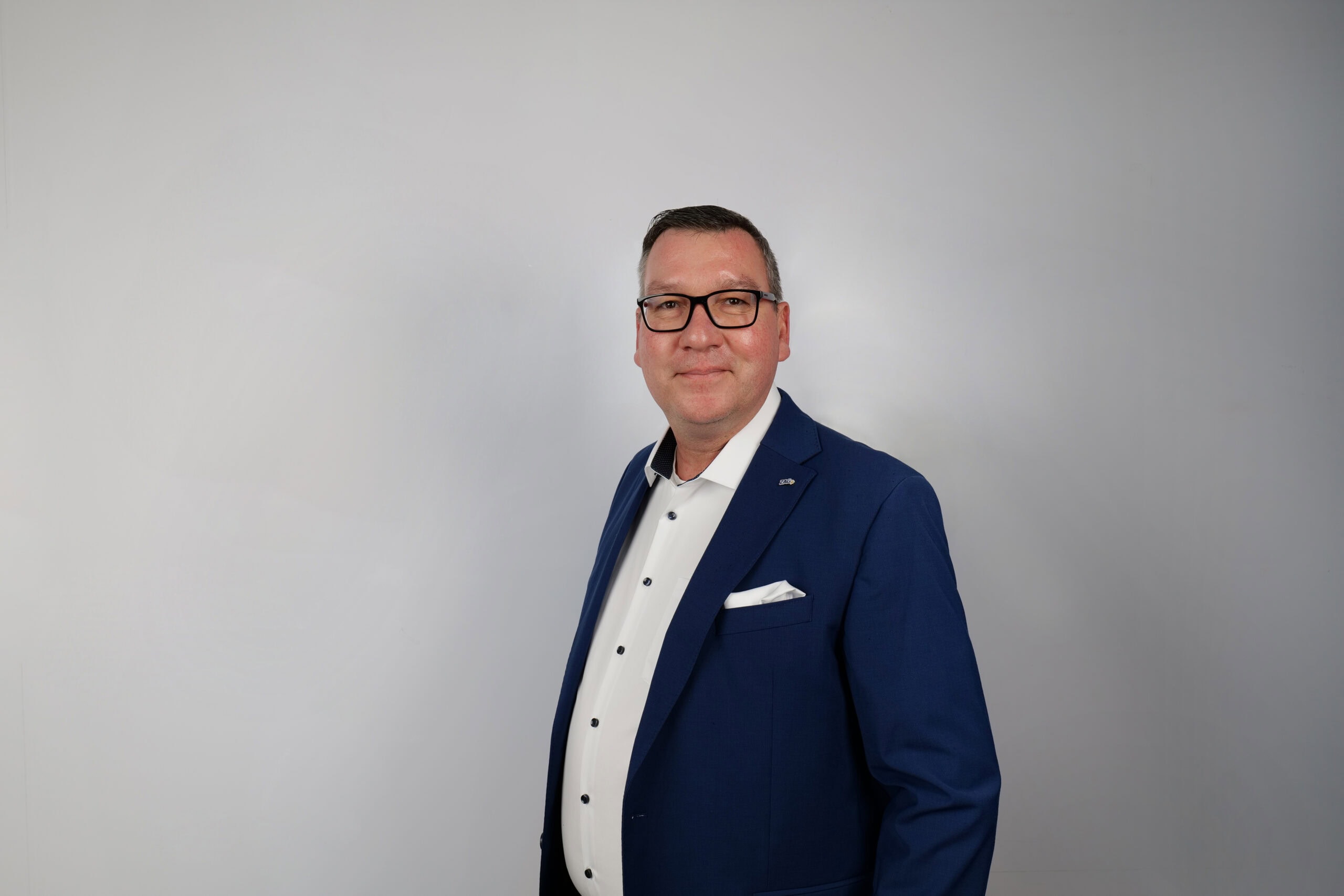 Mann in Businesskleidung vor neutralem Hintergrund, professionell und vertrauenswürdig, repräsentativ für ZAG Personalvermittlung und Arbeitsvermittlung, Fokus auf Karriere, Jobsuchende und Personalmanagement.